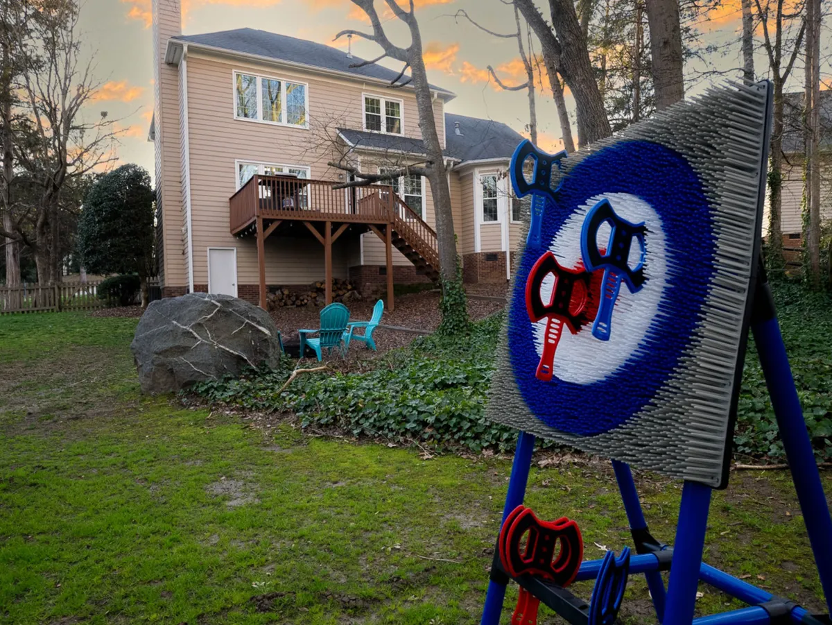 A backyard scene featuring a spacious deck connected to the house, with a comfortable seating area and a colorful axe target board for outdoor games. The atmosphere is cheerful and relaxed, inviting guests to gather for fun activities and socializing.