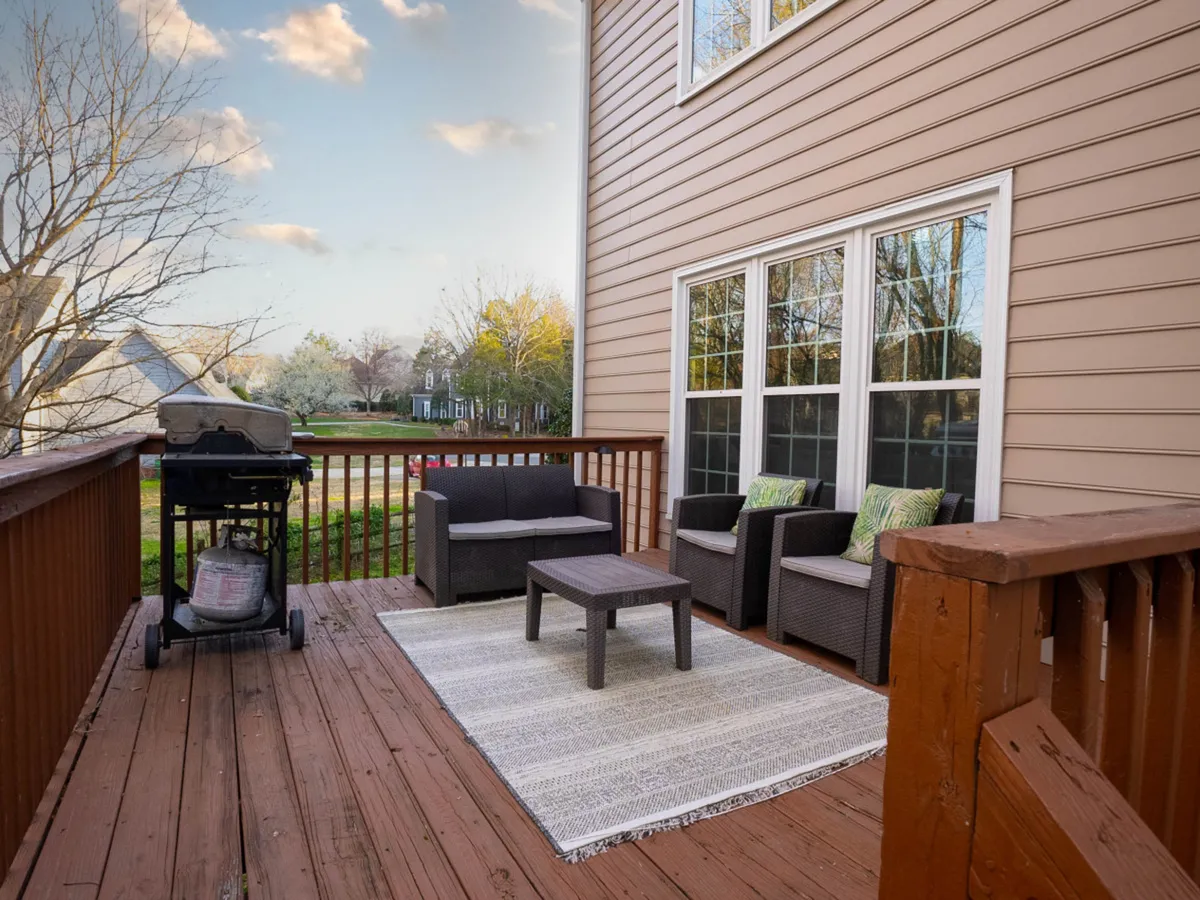 An exterior patio scene featuring a comfortable seating area, a grill, and an outdoor rug. The setup suggests a casual and friendly environment ideal for barbecuing, relaxing, and entertaining outdoors.