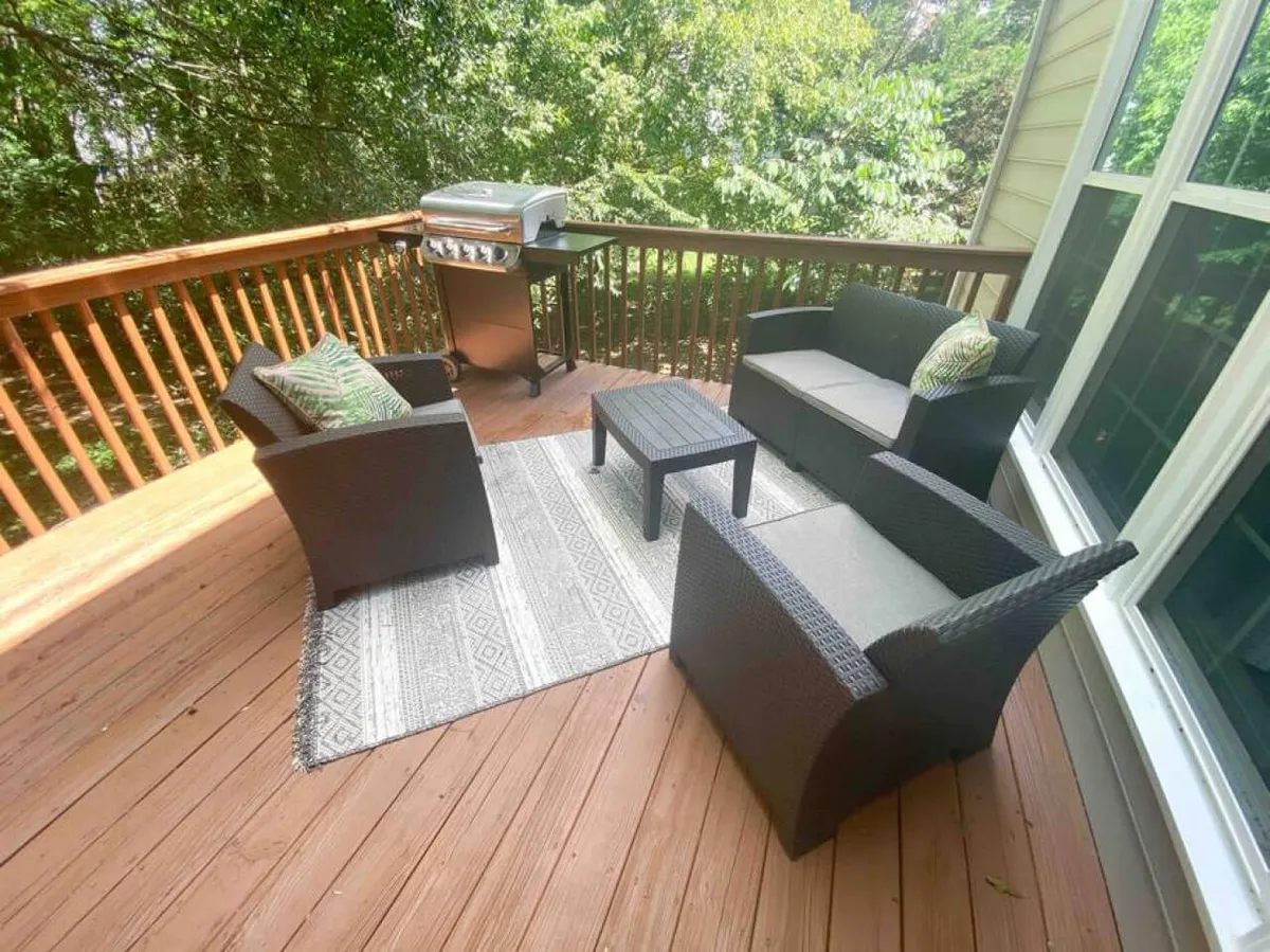 An outdoor seating area with a grill, decorative rug, and stylish furniture, set up for barbecuing, relaxing, and entertaining. The scene is casual and welcoming, ideal for hosting large gatherings or enjoying quiet moments.