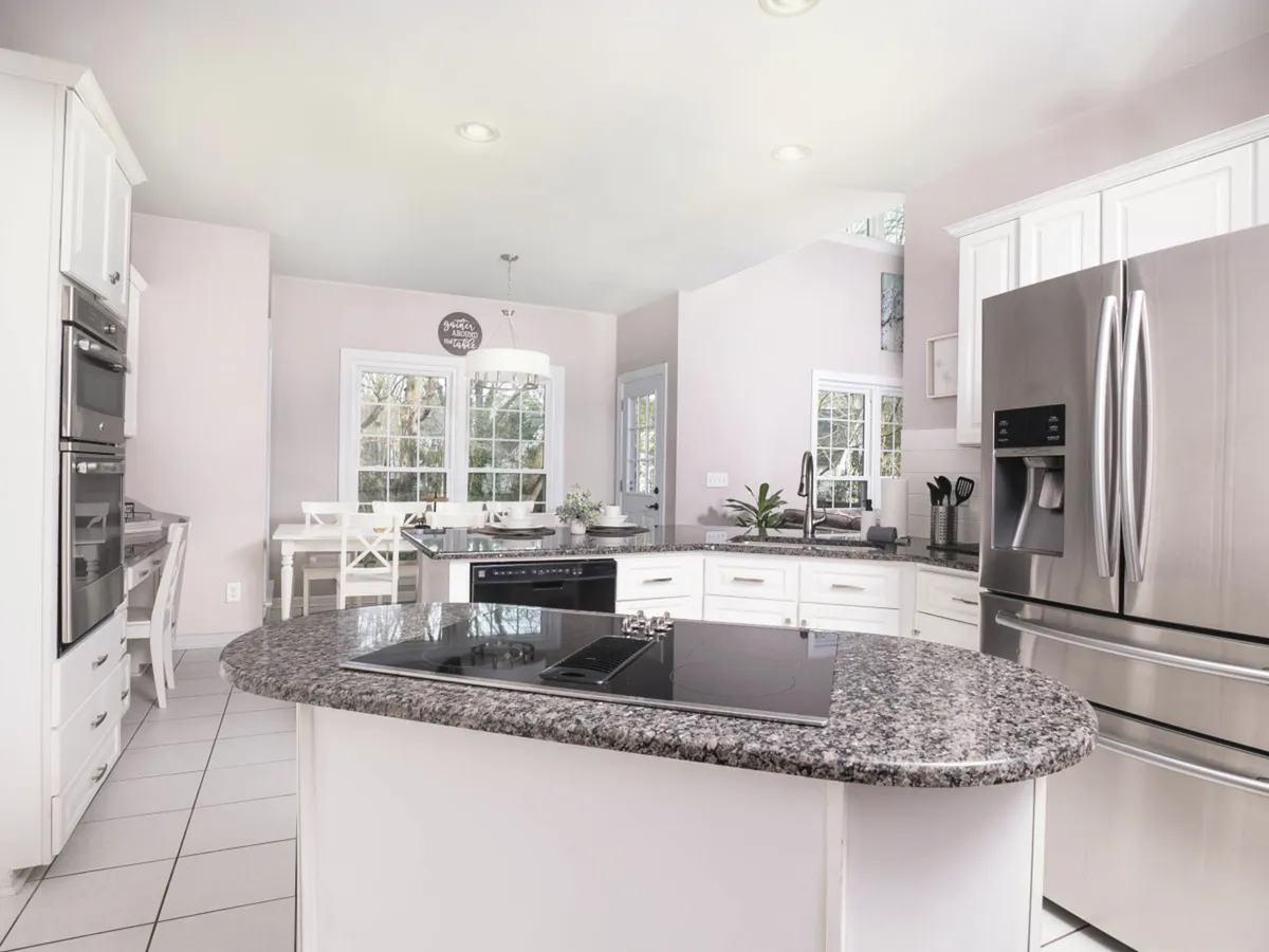 A spacious, light-filled kitchen with an island countertop, stainless steel appliances, bright windows, and an adjacent dining table. The setup is ideal for both cooking and gathering, with ample space for multiple people to work or socialize.
