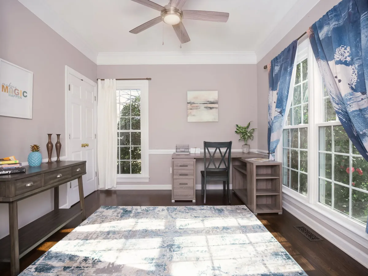 A dedicated home office setup with a desk, comfortable chair, window providing natural light, decorative wall art, and an area rug. The arrangement is both practical and aesthetically pleasing, inviting productivity in a tranquil setting.