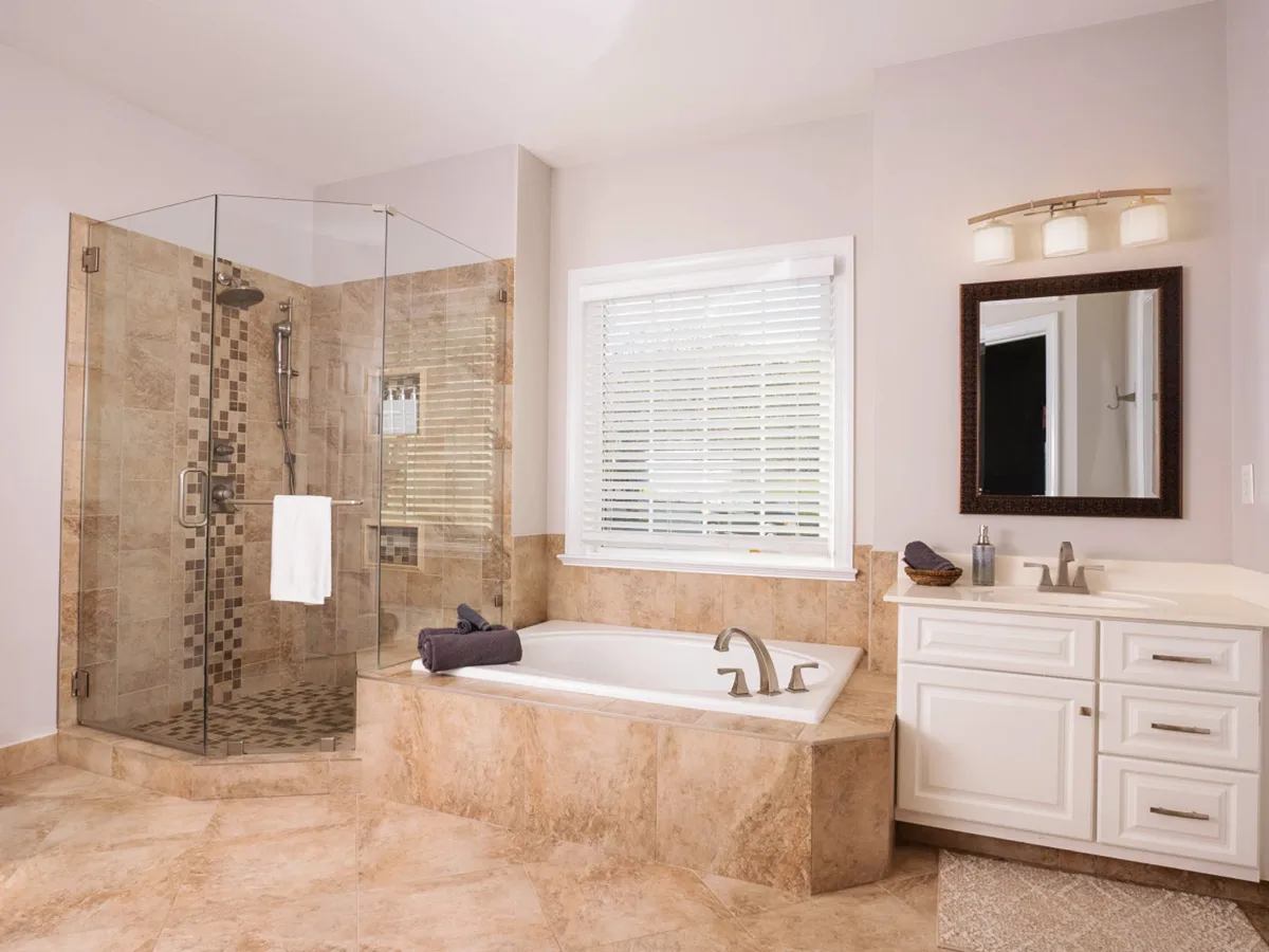 A luxurious bathroom featuring a glass shower enclosure, freestanding bathtub, double sink vanity, and a large window. The space feels open, spa-like, and filled with natural light, ideal for unwinding after a long day.
